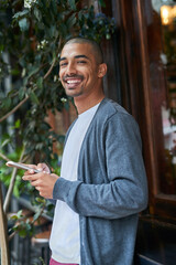 Just texting a friend to meet up with me. Portrait of a young man texting on his cellphone outside.