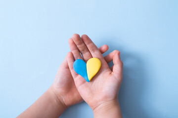 Heart of yellow-blue colors of the national flag of Ukraine in a childs hands, top view. Love for the motherland in the children's heart concept