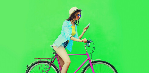 Summer colorful image of happy smiling young woman with smartphone riding on bicycle on vivid green background
