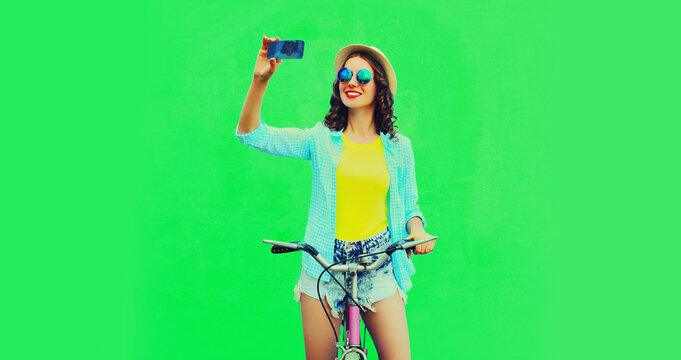 Summer colorful image of happy smiling young woman taking selfie by smartphone with bicycle on vivid green background