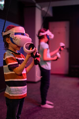 vr game and virtual reality. team kids friends gamers fun playing on futuristic simulation video game in 3d glasses and joysticks in entertainment vr room with innovation technology and neon light