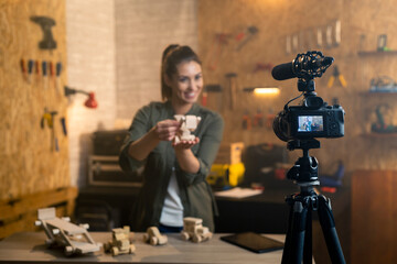 Woman in a carpentry workshop being filmed with a camera for a blog. Focus is on camera.