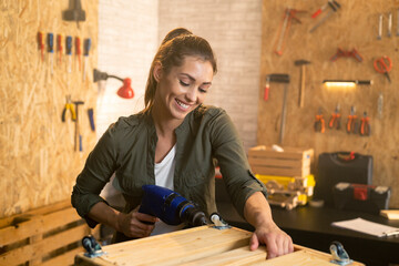 Woman carpenter working with drill in workshop