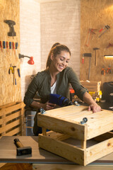 Woman carpenter working with drill in workshop