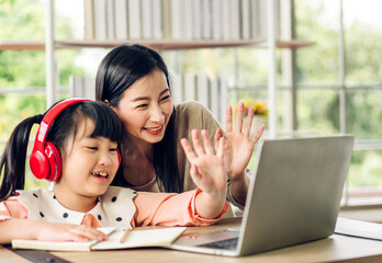 Mother and asian kid little girl learn and look at laptop computer reviewing lesson study with...