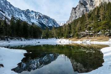 Fototapeta na wymiar Winter landscape of Austrian Alps with Green Lake in the middle. Powder snow covering the mountains and ground. Soft reflections of Alps in calm lake's water. Winter wonderland. Serenity and calmness