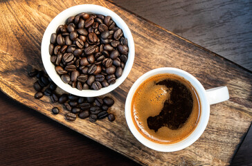 Close-up of hot black coffee in white coffee cup and roasted coffee beans in white bowl on wooden background. Top view 