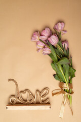a bouquet of pink tulips on a beige background and a wooden craft inscription love
