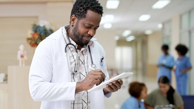 Black People Doctor With Gown Uniform Holding Digital Tablet In Hands To Write Medical Record Standing In Healthcare Center Working At Hospital