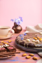 Homemade chocolate brownie cake with caramel cream and almonds with cup of coffee on a colored and pink background. Side view, selective focus, copy space.