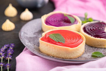 Sweet tartlets with jelly and milk cream with cup of coffee on a black concrete background. Side view, selective focus.