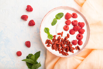 Yogurt with raspberry and goji berries in ceramic bowl on white concrete background. top view.