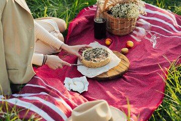Woman cutting pie on a picnic. Picnic setting with tart, cheese brie and red wine. Woman sitting on the green grass in a park.
