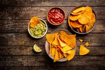 Two biowls of yellow corn tortilla nachos chips with salsa and guacamole sauce over wooden background, top view - obrazy, fototapety, plakaty
