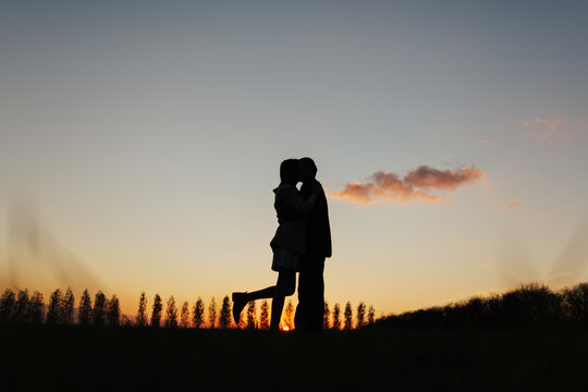 Silhouette of romantic couple of lovers while hug and kiss with colorful sunset sky on background. Copy space.