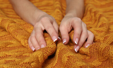 Woman touching soft orange knitted fabric, closeup view