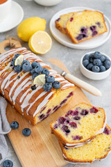 Lemon blueberry cake with lemon icing and fresh berries on top on the board on a gray concrete background with cup of tea. Selective focus. Copy space.