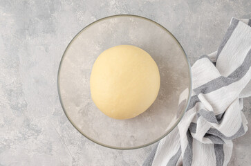 Raw yeast dough in a bowl on a gray concrete background. Dough for making sweet bread, brioche or...