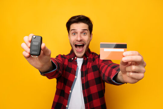 Excited Guy Showing Car Key And Credit Card, Yellow Background
