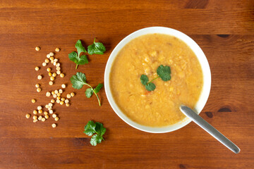 Yellow split pea lentil soup  in a bowl, garnished with corrinader leaves, with a spoon on a wooden table. Indian Dahl.  View from above.