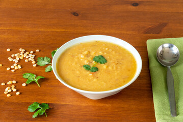 Yellow split peas lentil soup, garnished with coriander leaves, in a bowl with a spoon and napkin on a wooden table. Indian dahl. Copy space