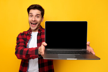 Excited young man showing black empty laptop screen