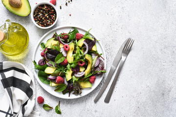 Mix salad with arugula, avocado and raspberries on a stone concrete background. View from above