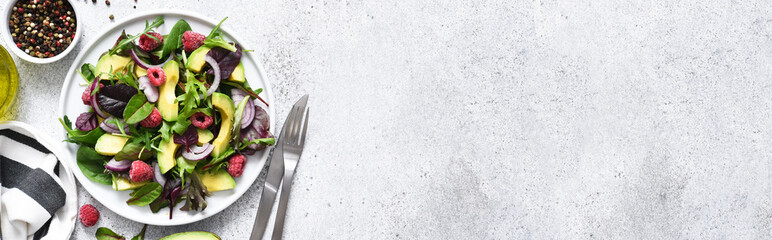 Mix salad with arugula, avocado and raspberries on a stone concrete background. View from above