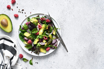Mix salad with arugula, avocado and raspberries on a stone concrete background. View from above