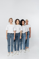 Fototapeta premium Full length of interracial women in jeans and t-shirts on grey background, feminism concept.