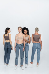 Obraz premium Full length of african american woman hugging blonde friend on grey background.