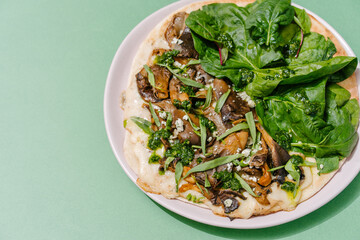 Italian Piadina with oyster mushrooms, spinach, pesto, mozzarella, bechamel, gorgonzola cheese, green onions. Green background. Copy space