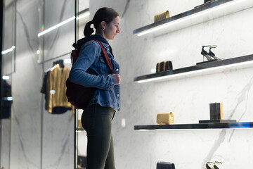 Woman stands at a boutique window and looks at shoes.