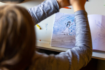 Little girl paints a picture with crayons. Photo taken in natural light from the window.