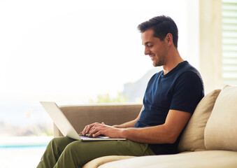 Spending some of his well earned free time online. Shot of a handsome young man using his laptop while sitting on the sofa at home.