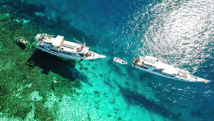 Top down drone shot of two boats anchored in one of the bays of Komodo National Park, Flores, Indonesia. The sea is crystal clear, shining with turquoise and blue shades. Island hoping