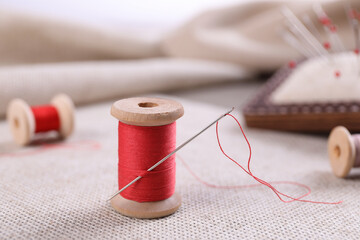 Spool of red sewing thread with needle on white fabric