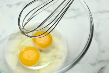 Whisking eggs in glass bowl on white marble table, closeup