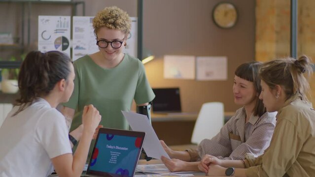 Young woman with prosthetic arm discussing business project with team of female colleagues while brainstorming at office meeting
