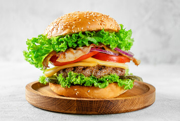American food concept. Burger with beef and bacon on wooden plate on gray background.