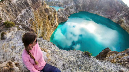 Woman sitting at the volcano rim and watching the Kelimutu volcanic crater lakes in Moni, Flores, Indonesia. Woman is relaxed and calm, enjoying the view on lake shining with many shades of turquoise