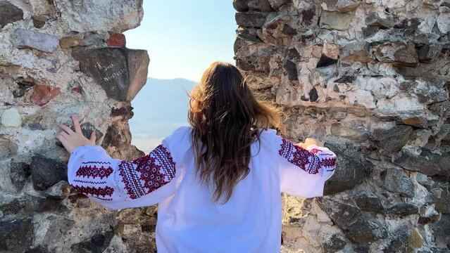 Ukrainian girl in an embroidered shirt against the background of a ruined fortress worries about the war around the mountain of devastation and hope for the best in the eyes of sadness, reproach
