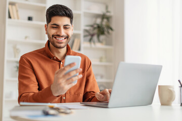 Portrait of smiling man using smartphone and pc at home - Powered by Adobe