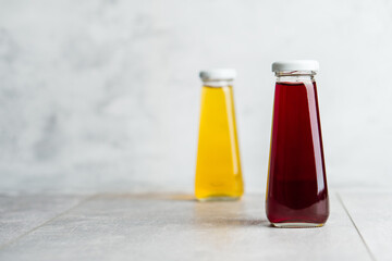 Bottles with yellow and red liquid halthy beverage on gray background. Orange and cherry juice