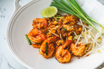 Shrimps Pad Thai or traditional Thai noodle menu, Pad Thai in stylish round shape white plate on marble table, close up image Thai food.