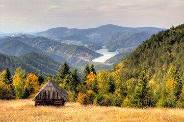 Wooden house in the mountains against the backdrop of a fantastic landscape. Autumn forest in yellow tones. Mountain lake in Serbia. Tara National Reserve. - obrazy, fototapety, plakaty