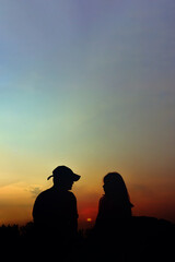 two silhouettes of people facing each other in front of a sunset.