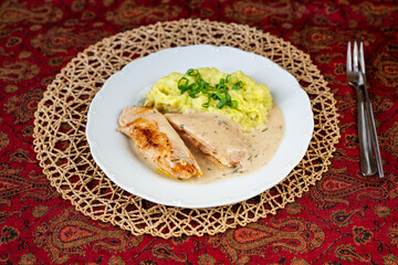 Chicken pocket stuffed with cheese and ham, rosemary sauce, mashed potato with pea on white plate on red.
