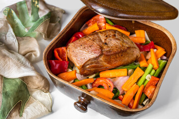 Baking pork neck on pile of orange and green raw vegetable in pan.