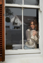Small town yearning. Shot of a young woman looking out through a rustic farmhouse window.